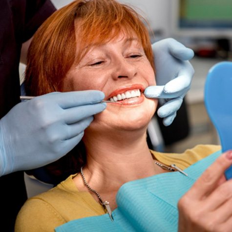older woman smiling while looking in dental mirror